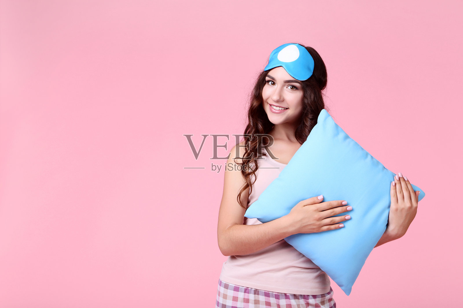 美丽女孩戴着睡眠面罩，枕头旁边，背景为粉色照片摄影图片