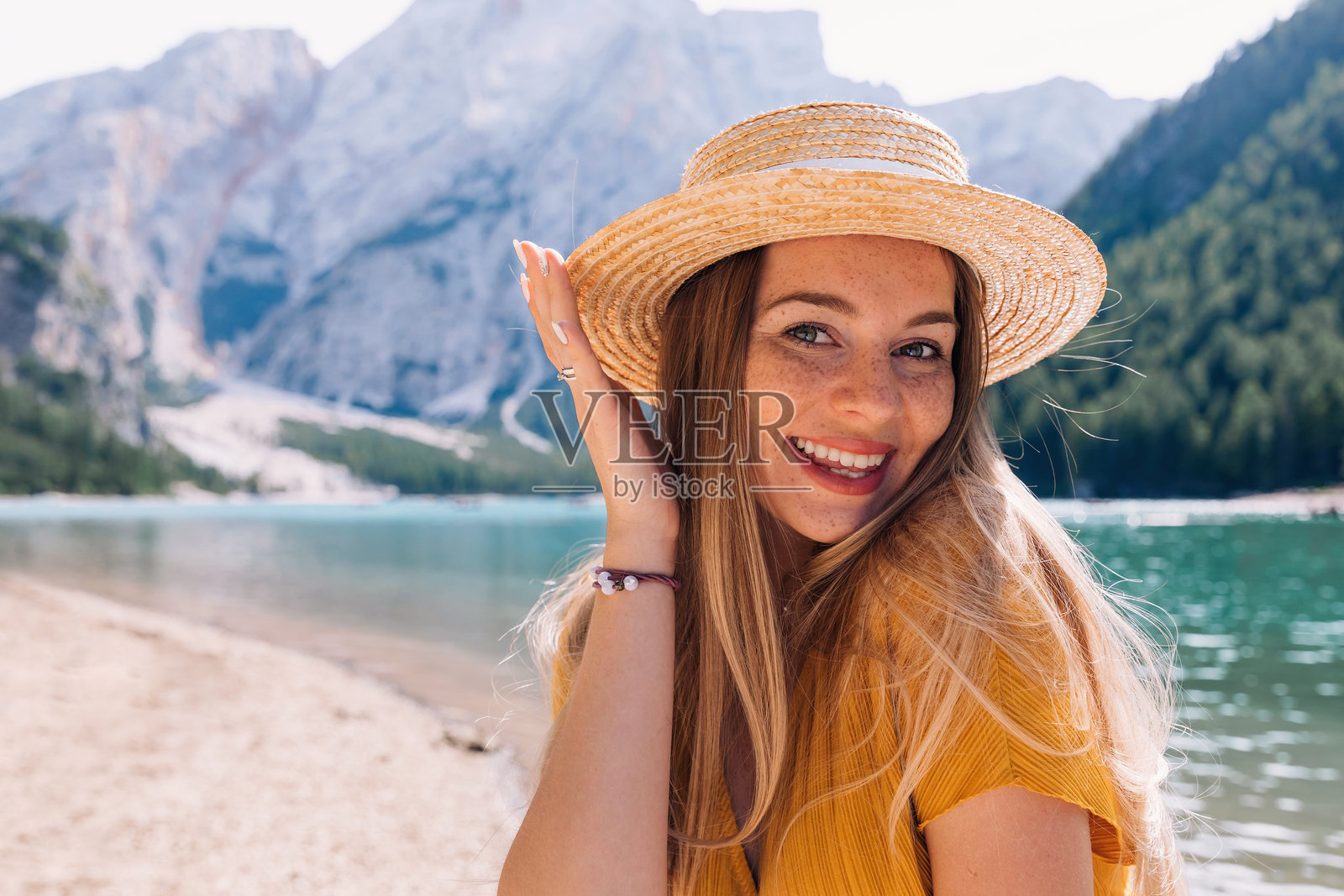 特写镜头下的女孩，脸上有雀斑，微笑着看向镜头，背景是岩石山脉和湖泊。意大利多洛米蒂山。照片摄影图片