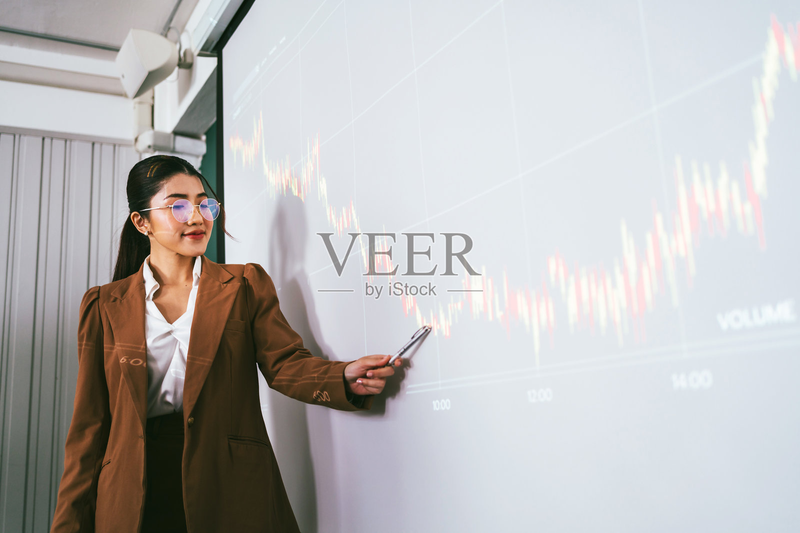 身穿棕色西装的亚洲泰国女商人在现代办公室展示财务图表，分析市场趋势。商业战略、领导力和数据分析的概念。照片摄影图片