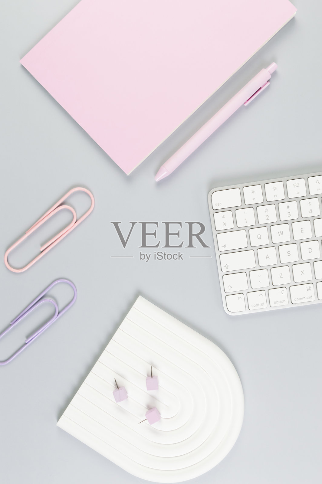 灰色背景上白色键盘、粉色笔记本、粉色钢笔的俯视图。纸夹、图钉，现代办公室，学校。照片摄影图片