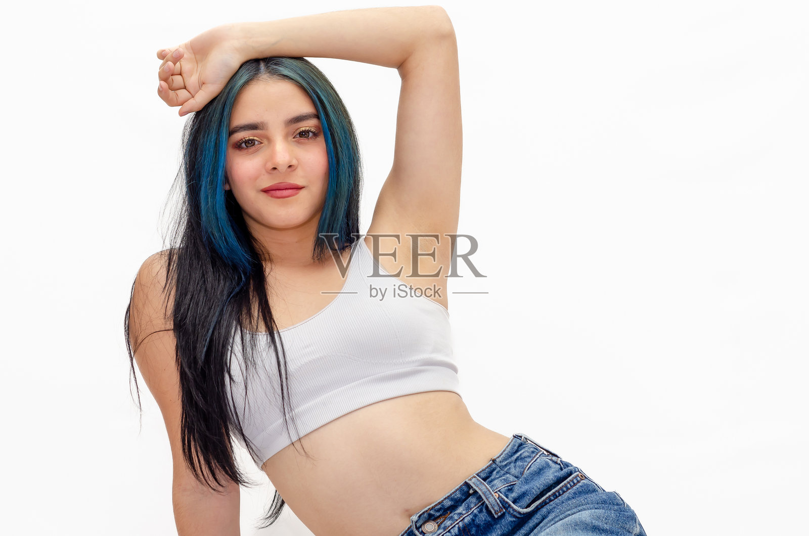 穿着运动胸罩和牛仔裤的美丽年轻女性，染着蓝色头发，背景为白色。照片摄影图片