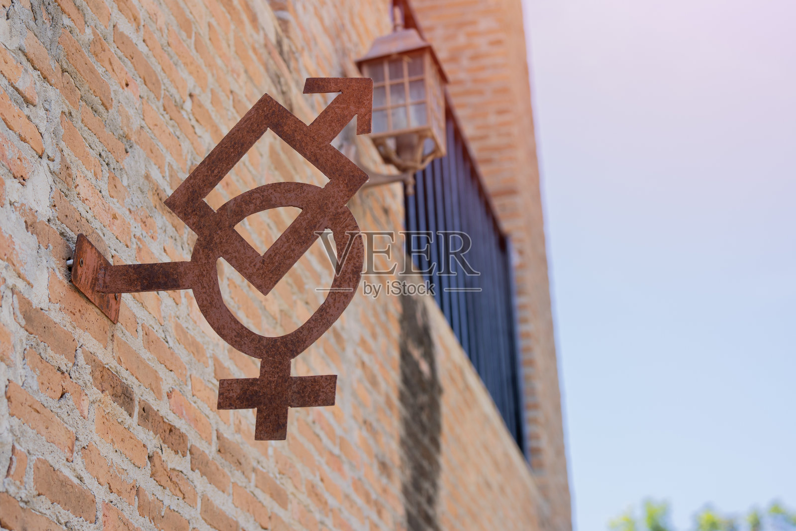 旧锈蚀的钢制厕所性别标志挂在古朴的橙色砖墙上照片摄影图片