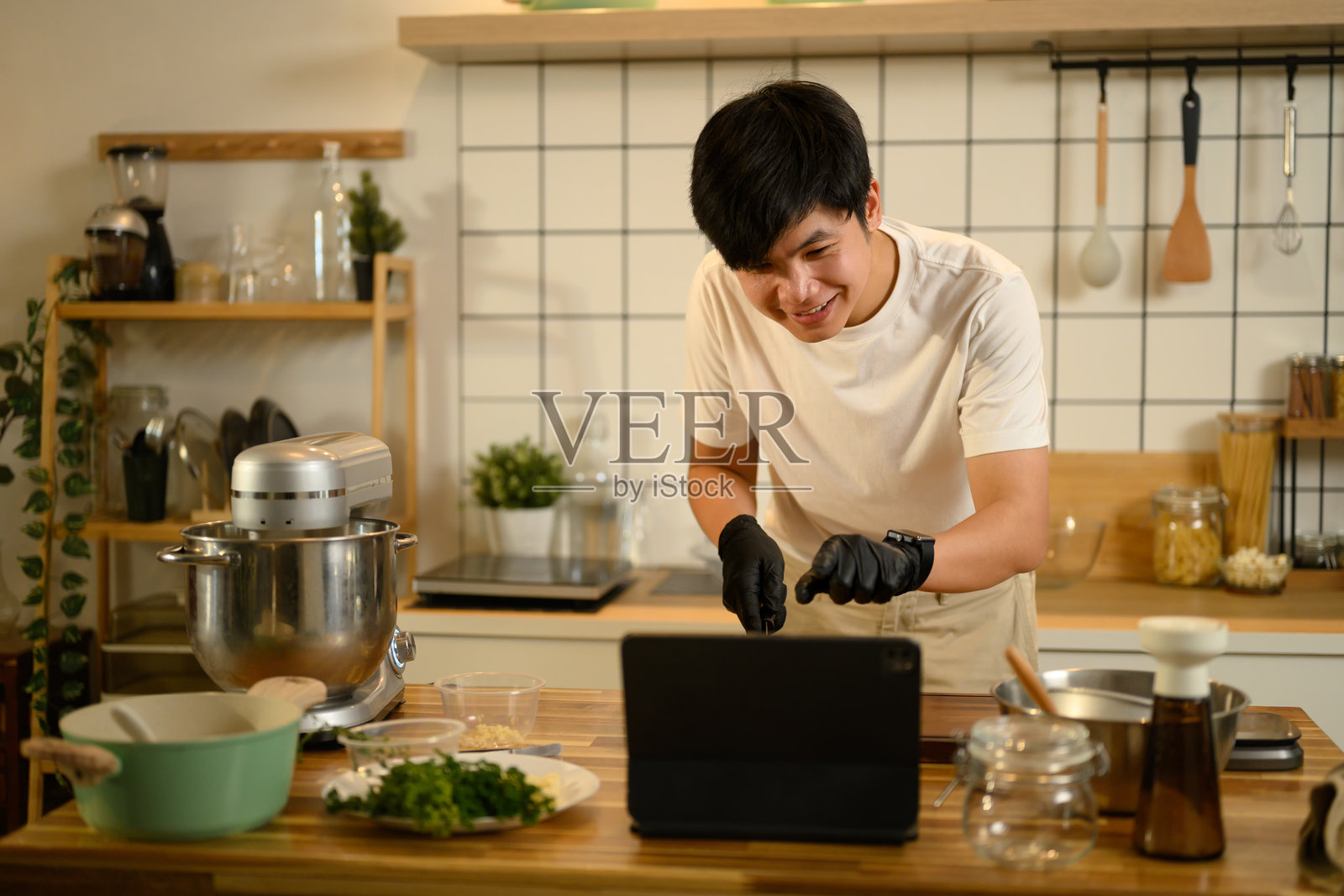 微笑的亚洲男子在准备打发奶油时，跟随数字平板上的在线食谱。照片摄影图片