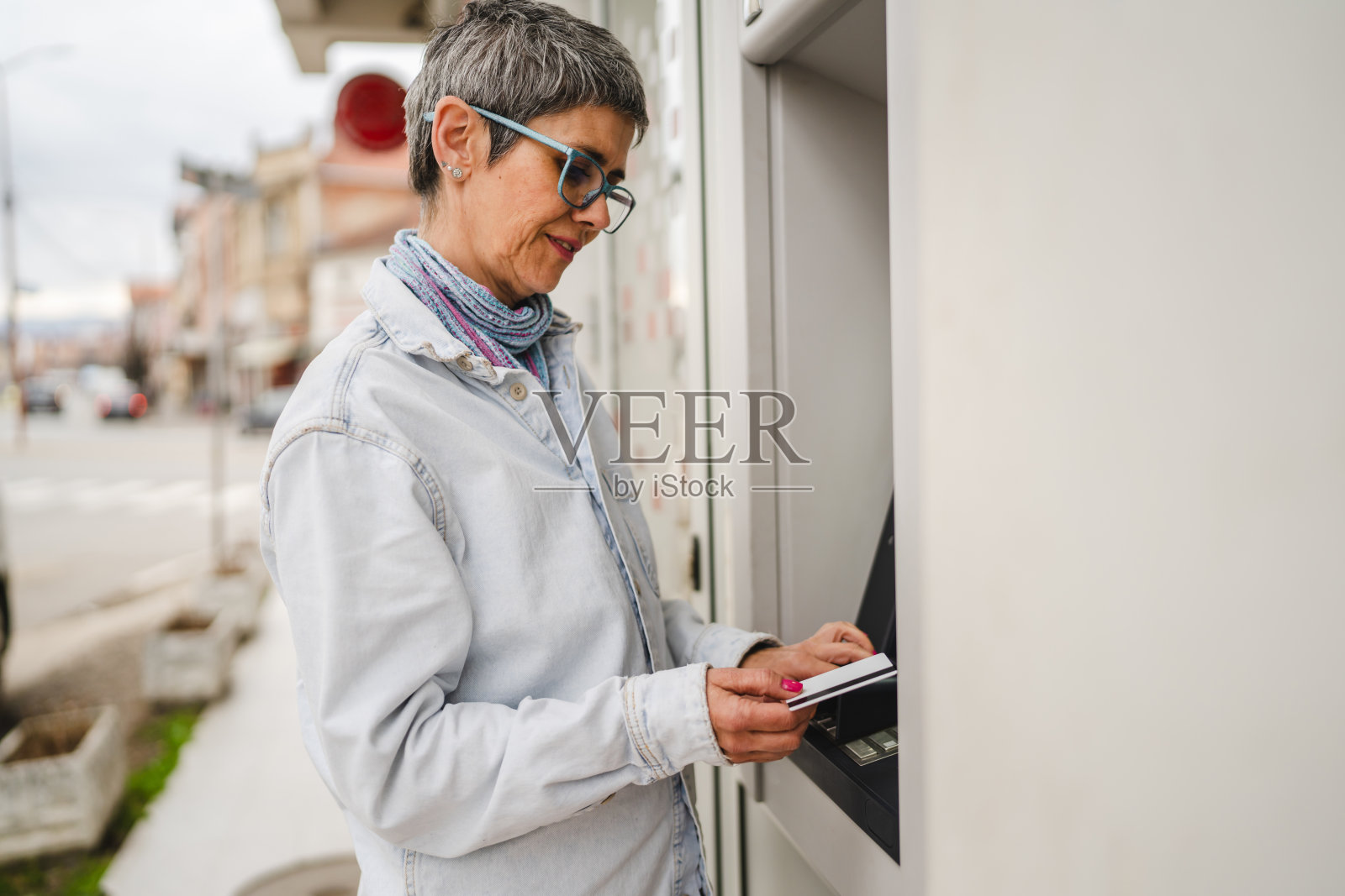 成熟的女性在户外使用信用卡提取现金于自动取款机照片摄影图片