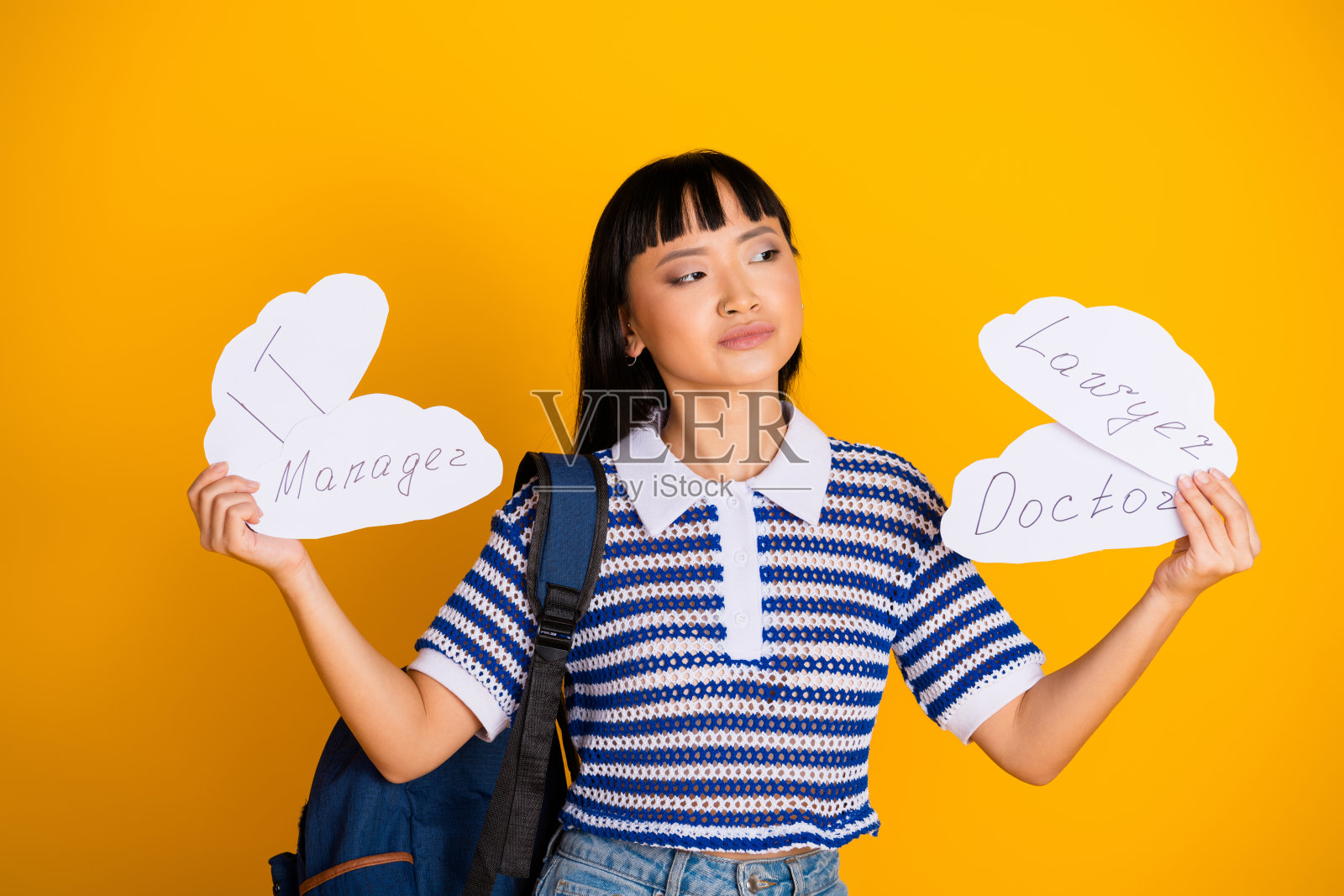 年轻女性在充满活力的黄色背景下思考职业选择，手持IT、医生和律师职业的标志。照片摄影图片