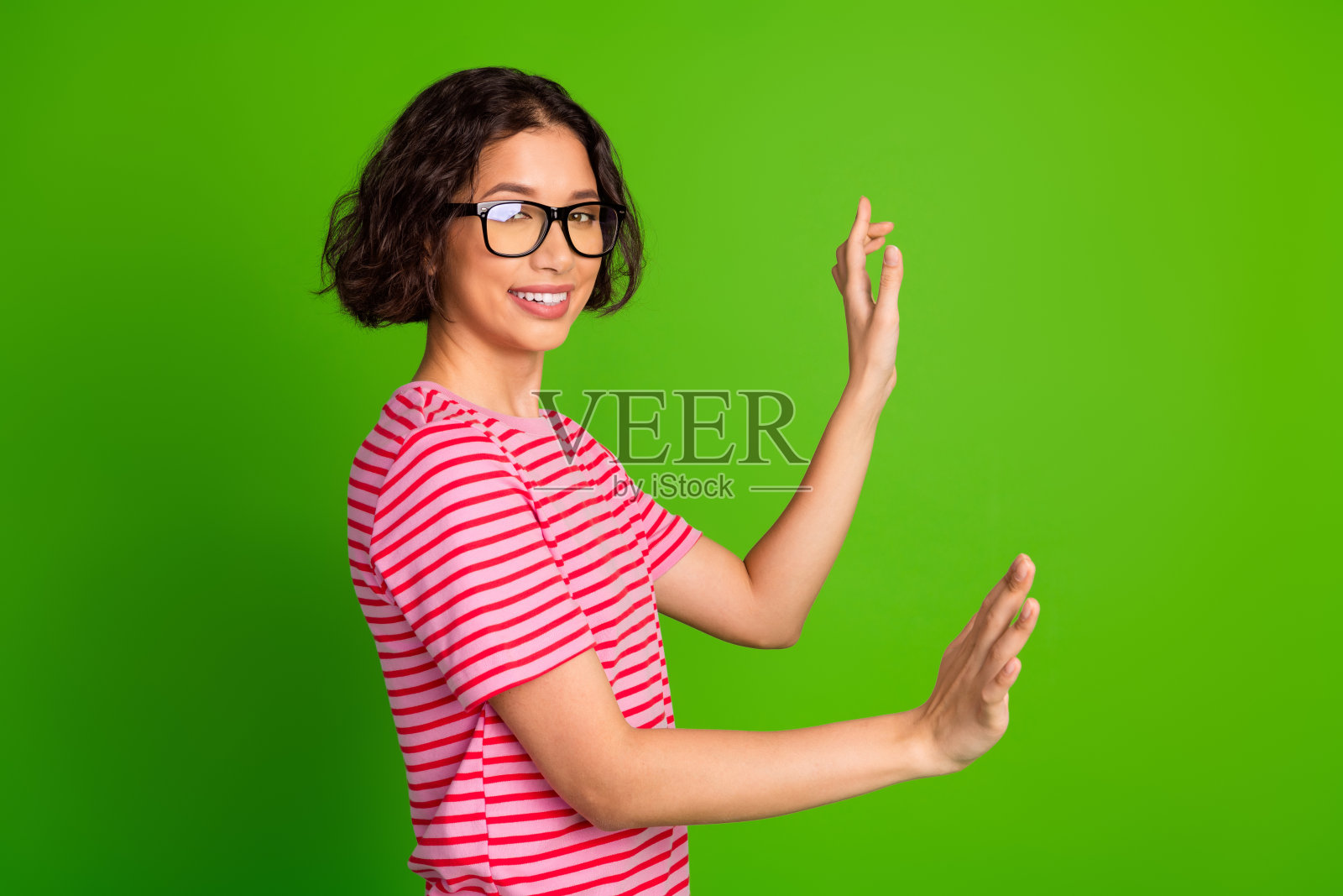 身穿条纹T恤的年轻女性在生动的绿色背景下用手势表达，散发出自信与风格。照片摄影图片