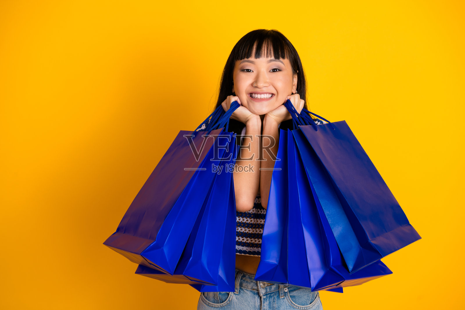 快乐的年轻女性在充满活力的黄色背景前微笑着，手里提着多个购物袋，庆祝她的购物狂欢。照片摄影图片