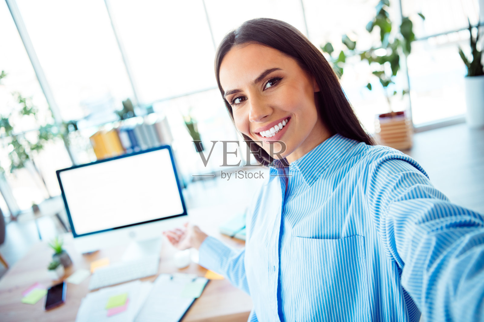 自信的职业女性在现代明亮的办公室环境中拍摄愉快的自拍，展现出快乐的心情照片摄影图片