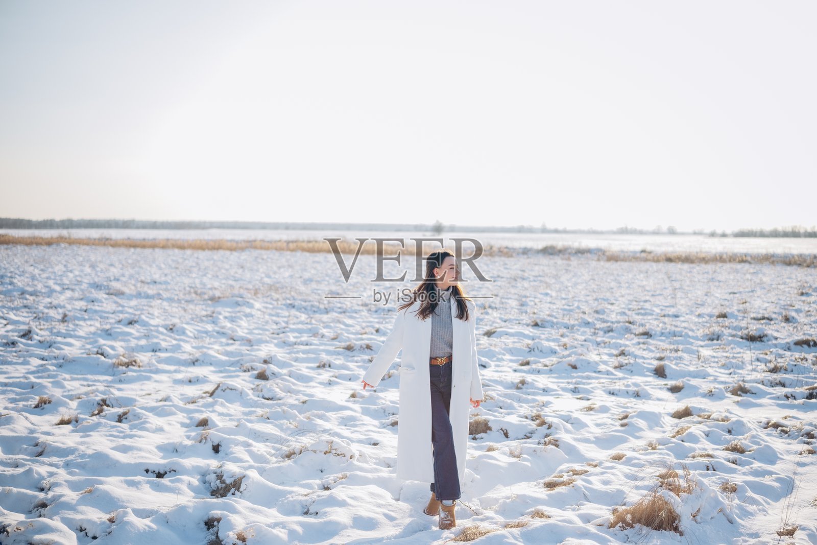 快乐的年轻女性在冬日阳光下走在被雪覆盖的草地上。照片摄影图片