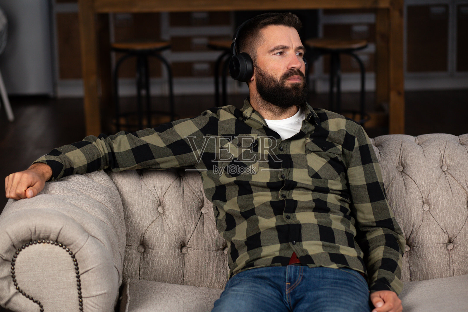 戴着耳机的胡子男人坐在沙发上，深思熟虑照片摄影图片
