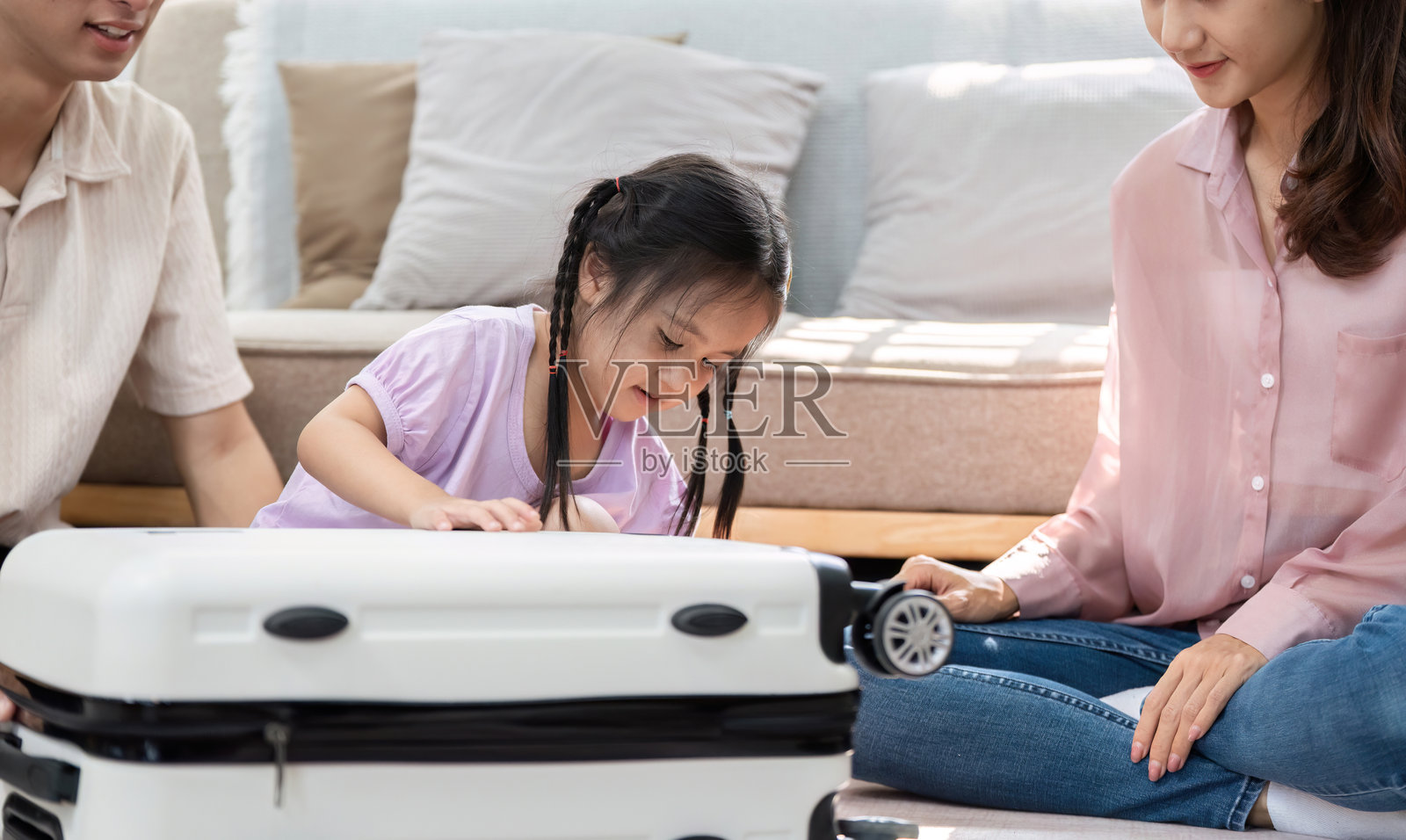 家庭亲密与旅行准备。一个年轻女孩快乐地探索一个行李箱，而她的父母与她互动。照片摄影图片