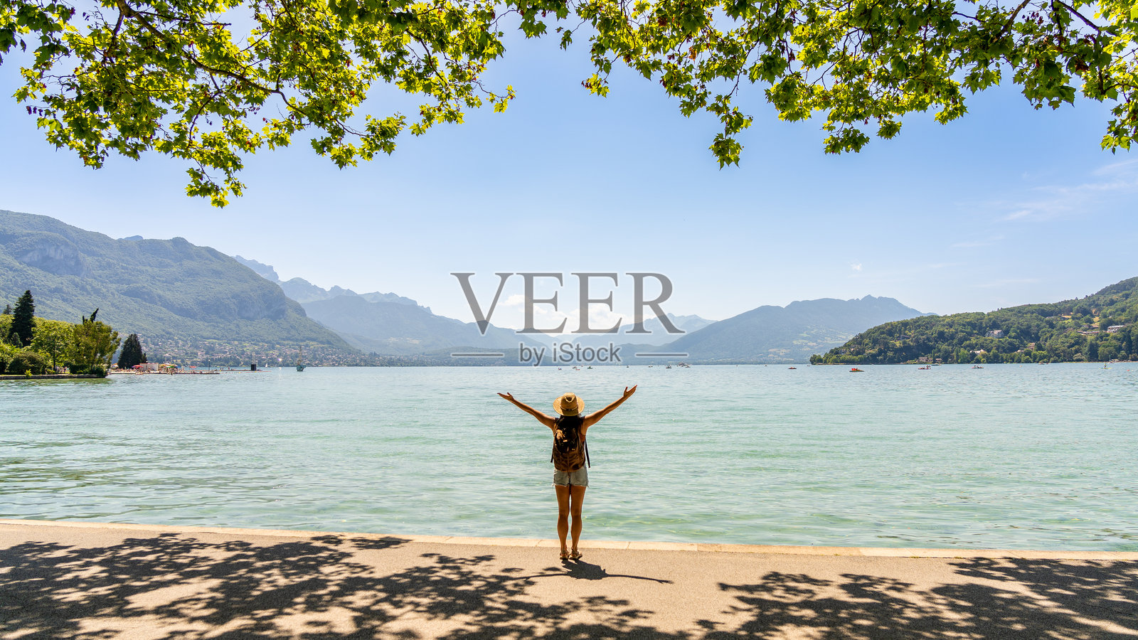 戴着帽子、背着背包、双臂交叉的女性站在高山湖泊前照片摄影图片