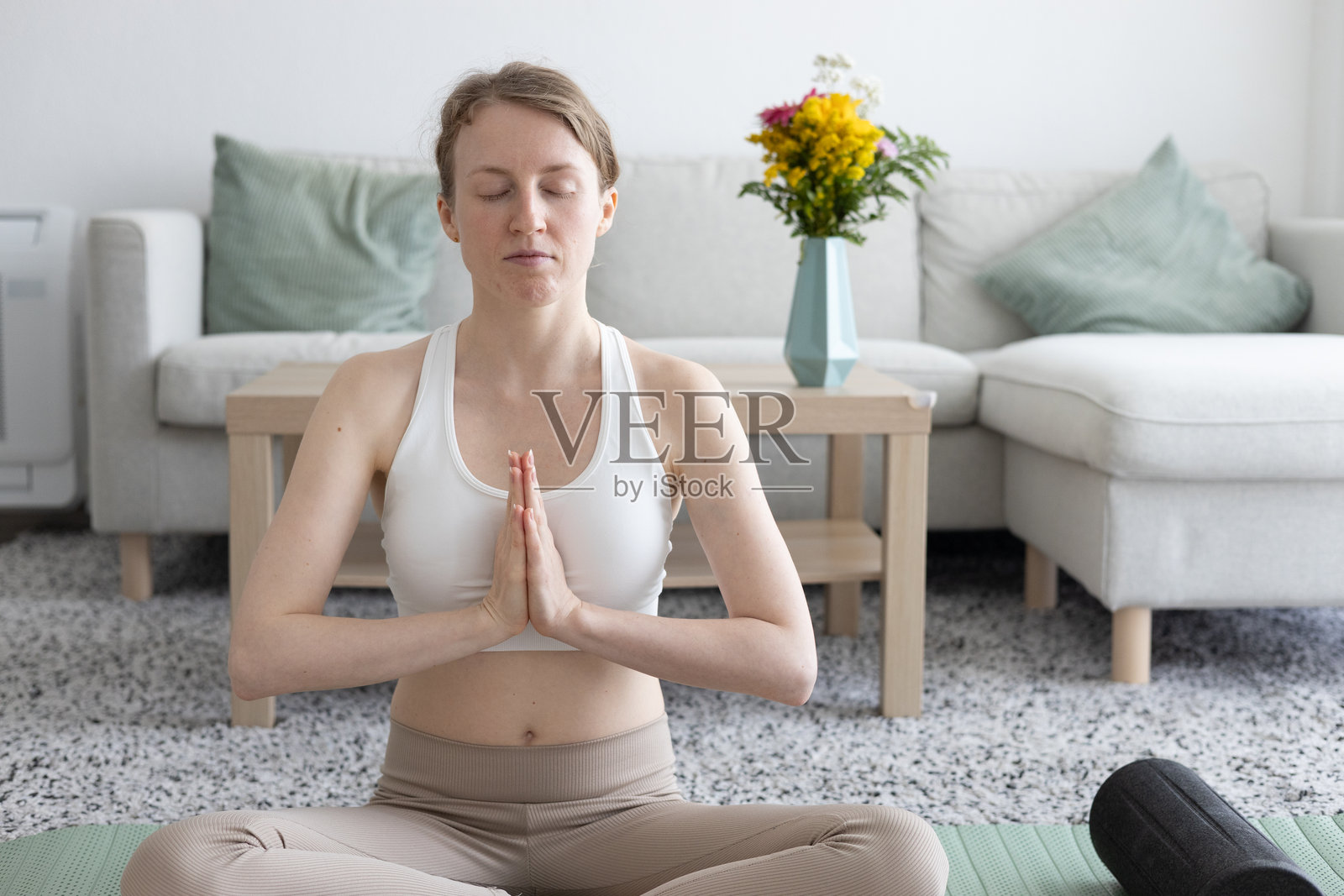 年轻女性在客厅里做瑜伽普拉提，旁边有舒适的沙发和装饰品照片摄影图片