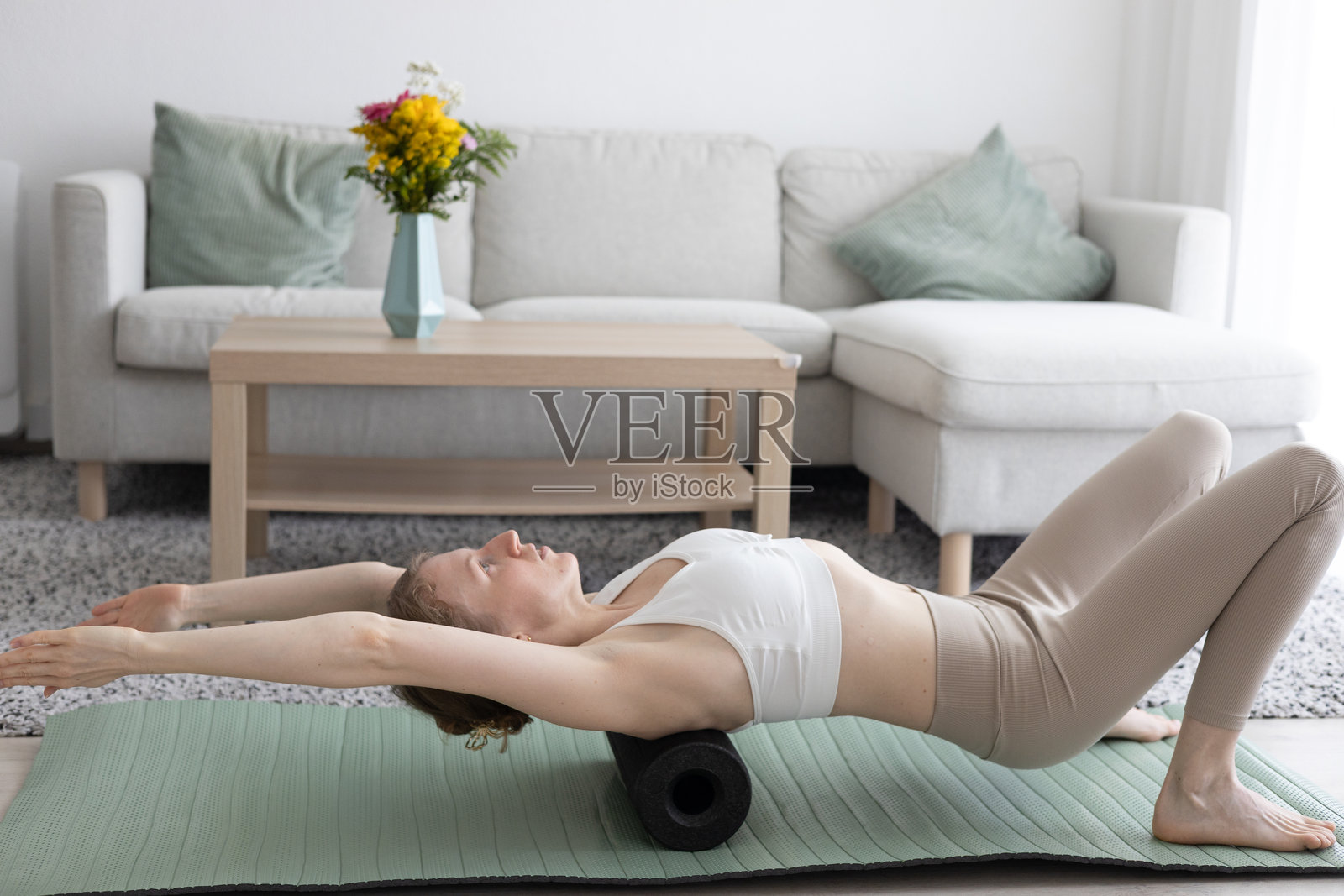 年轻女性在客厅里做瑜伽普拉提，旁边有舒适的沙发和装饰品。照片摄影图片