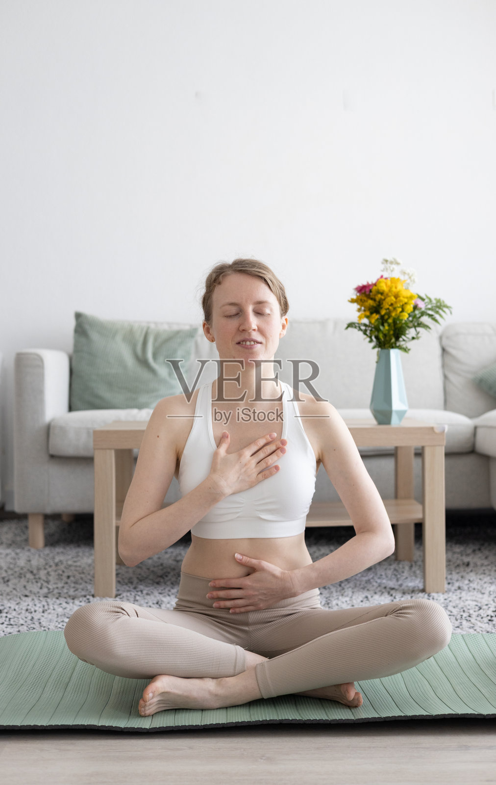 年轻女性在客厅里做瑜伽普拉提，旁边有舒适的沙发和装饰品照片摄影图片