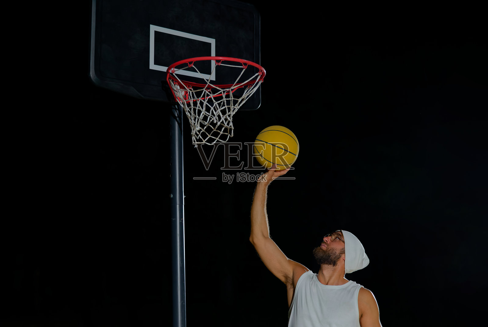 一名男子在夜晚的篮球场上，在明亮的户外灯光下完成扣篮。照片摄影图片