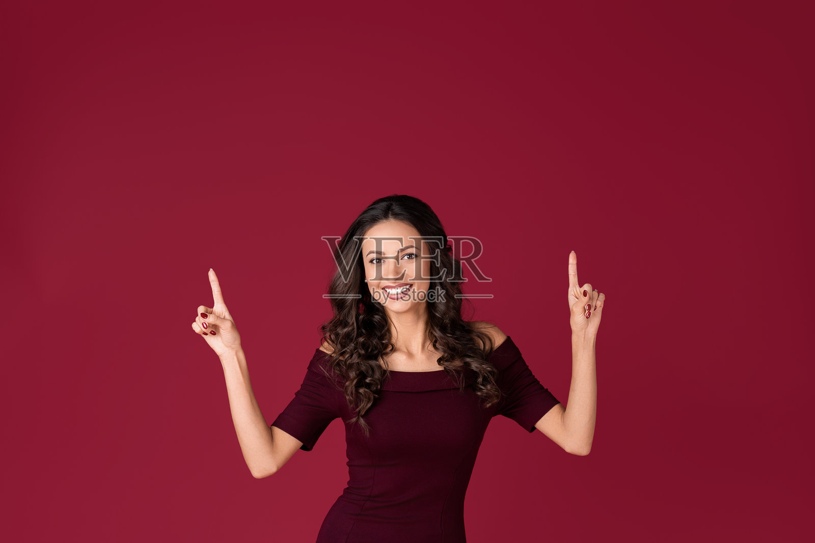 迷人的年轻女性穿着深红色连衣裙，手指指向红色背景。照片摄影图片
