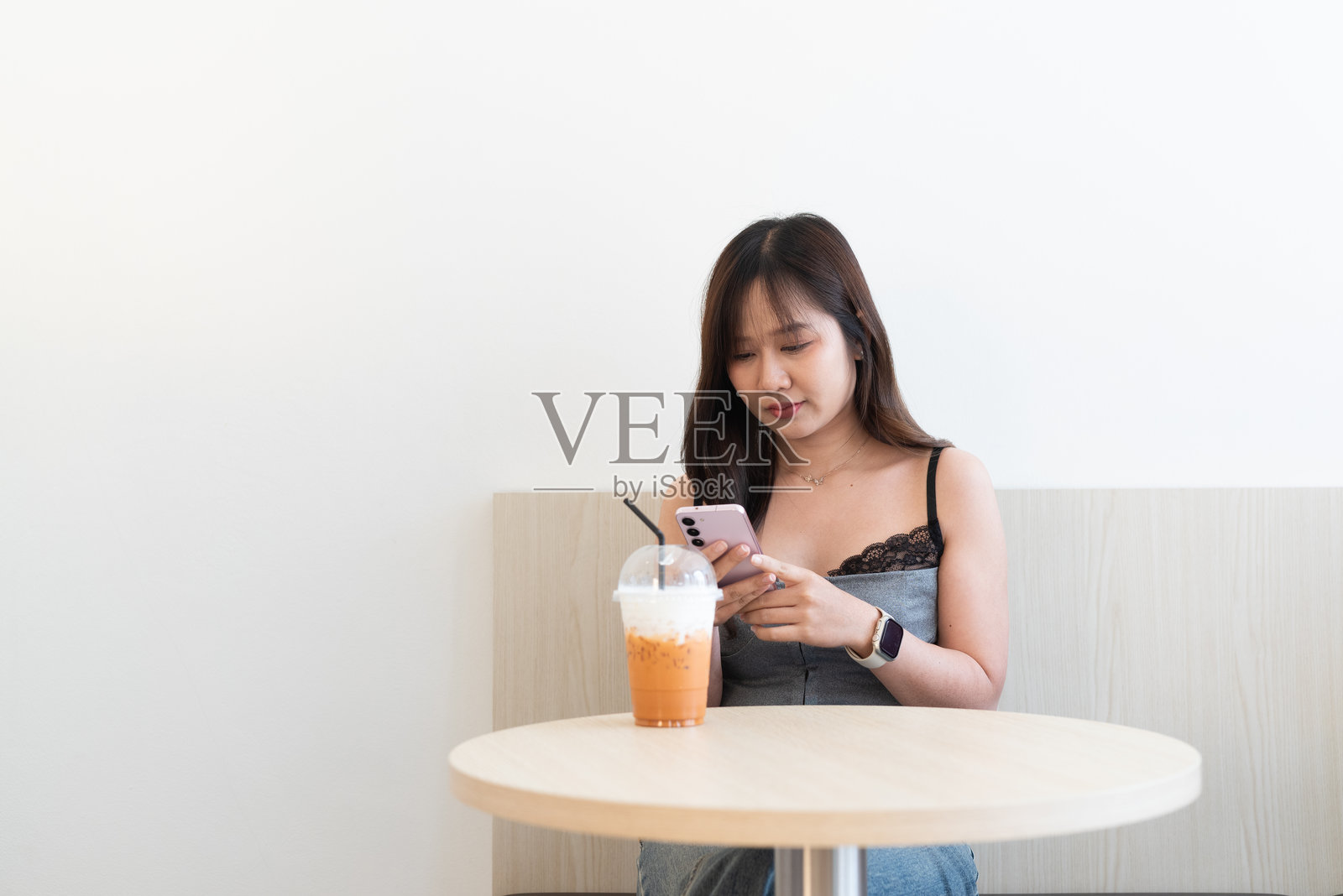 美丽的亚洲女性在咖啡店里喝泰式奶茶，同时使用手机照片摄影图片