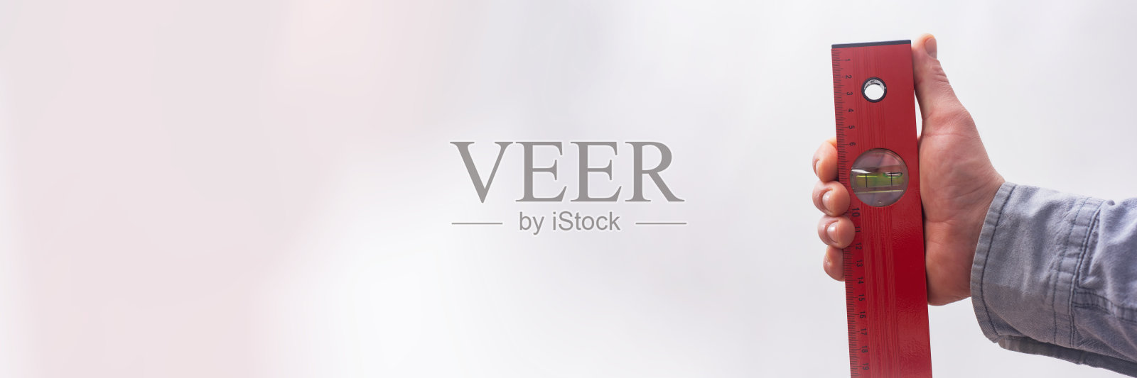 男性建筑工人手持红色水平仪，这是一种用于建筑和修理工作的精密工具。精准和建筑项目的概念。照片摄影图片