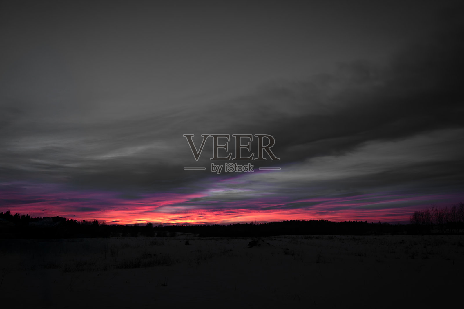 戏剧性的日落映照在雪-covered的风景上，森林轮廓若隐若现照片摄影图片