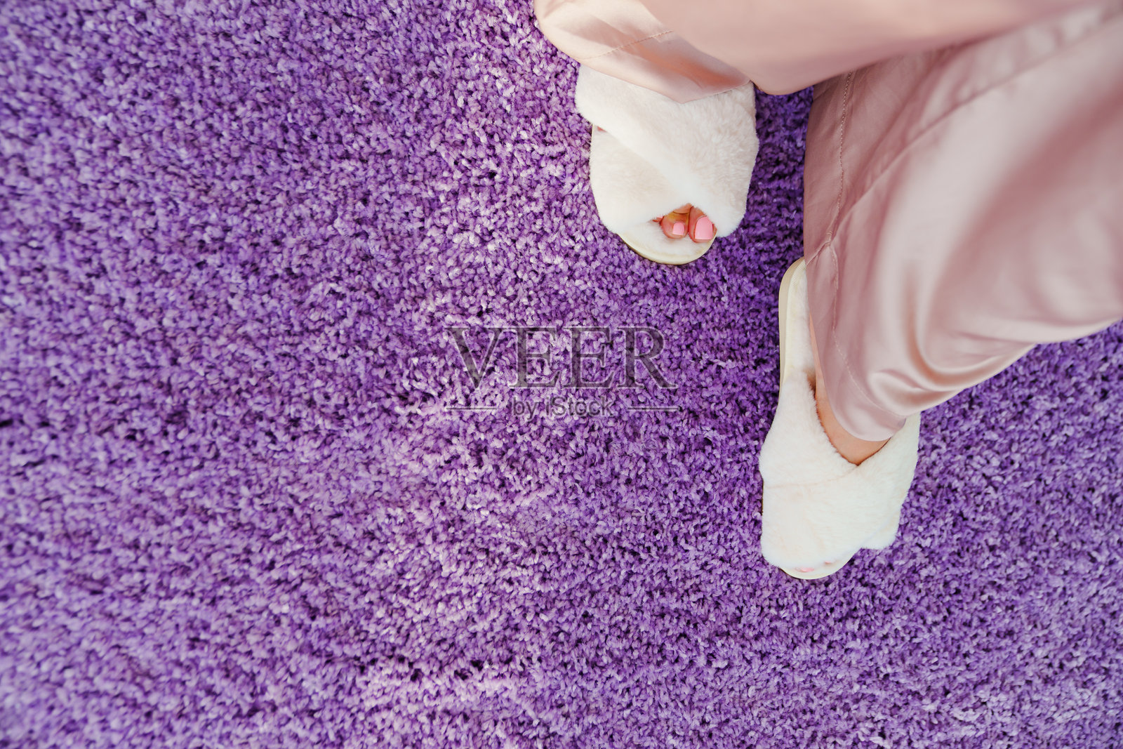 柔软的白色拖鞋放在紫色室内绒毛地毯上。照片摄影图片