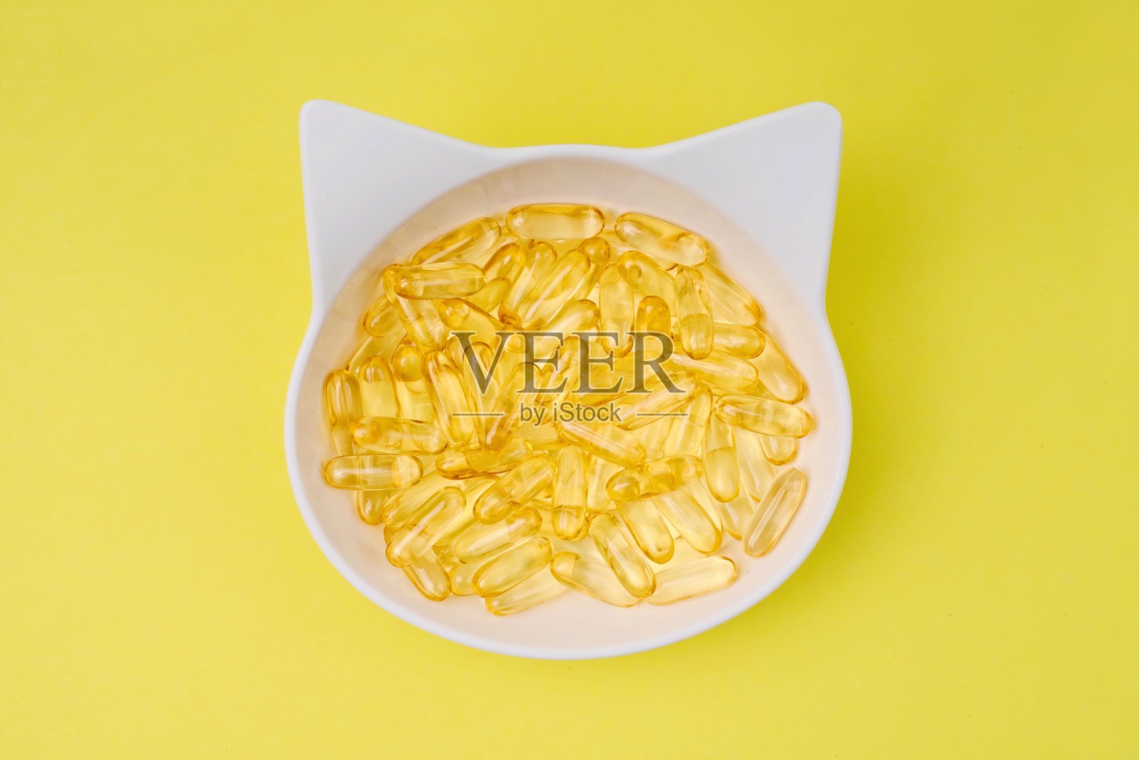 高角度视图的喂食碗，装满了鱼油Omega-3胶囊，背景为黄色。照片摄影图片