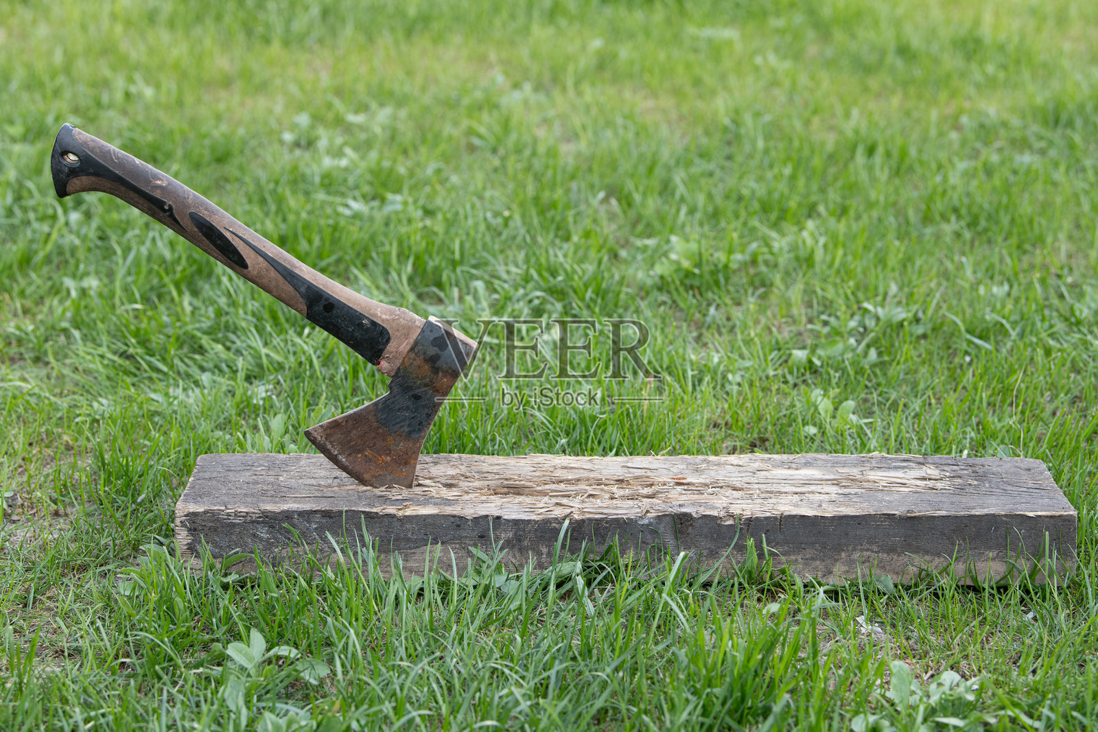 一把斧头卡在放置在绿草上的木块中，展示了户外劈木时的暂停。环境宁静自然，非常适合木工任务。照片摄影图片