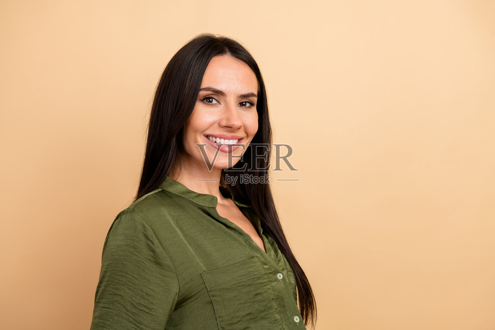 穿着绿色衬衫的职业年轻女性在米色背景前自信微笑，展现优雅与精致。照片摄影图片