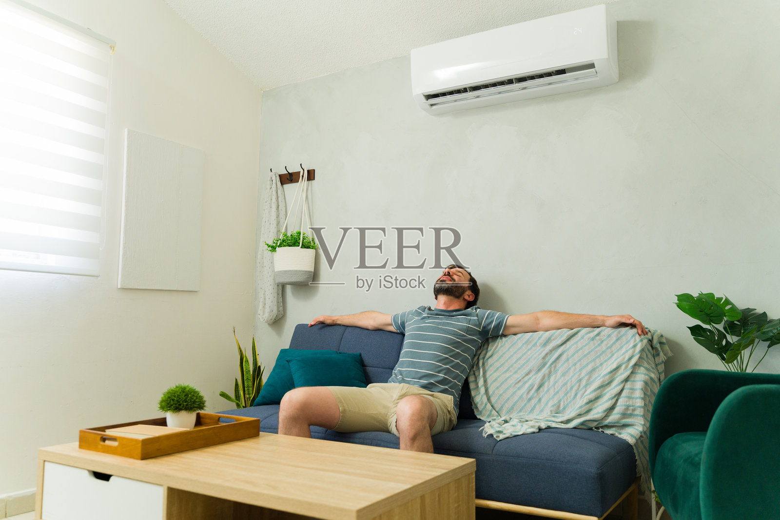 帅气的男人在家中沙发上放松，空调正对着他。照片摄影图片