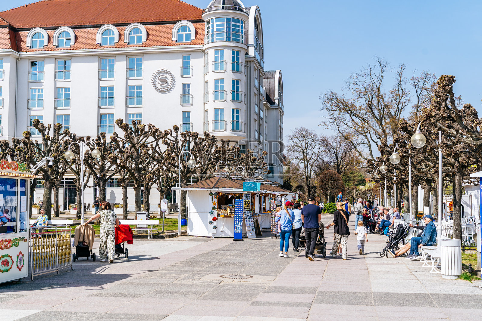树木成行的人行道，修剪整齐的树枝通向索波特大酒店，人们在走动和坐在长椅上。照片摄影图片