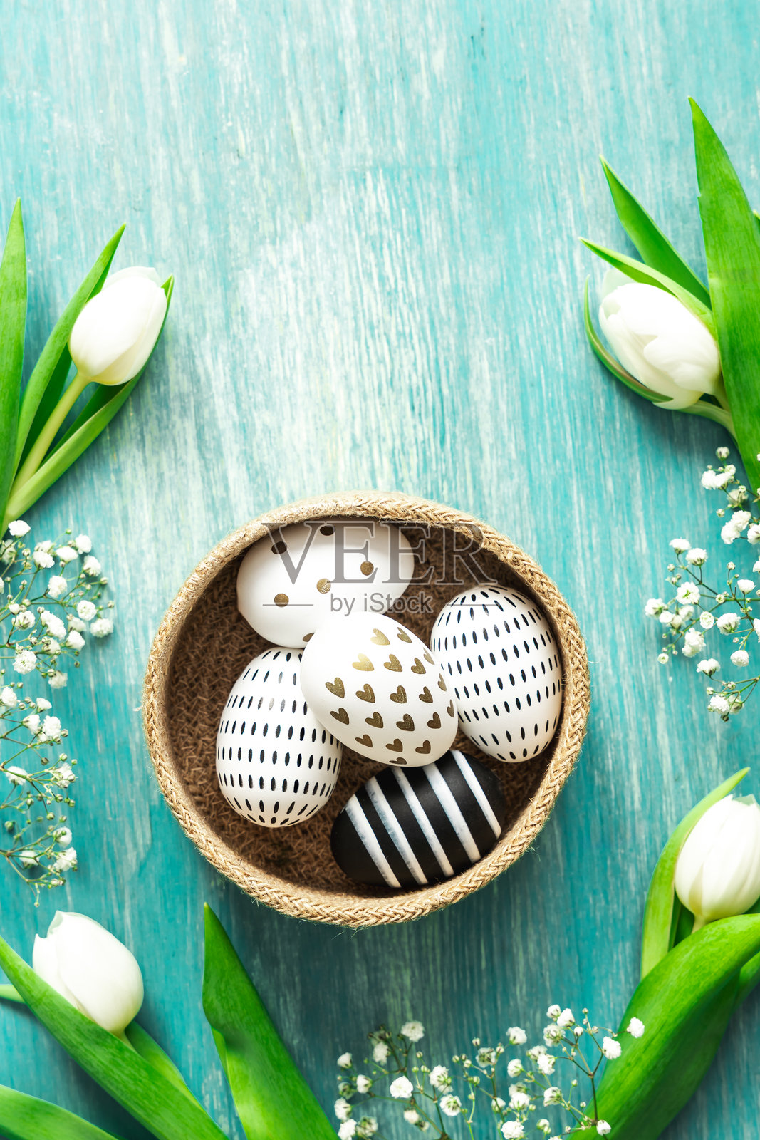 篮子里的复活节彩蛋，周围是白色郁金香，放在青绿色的桌子上。照片摄影图片