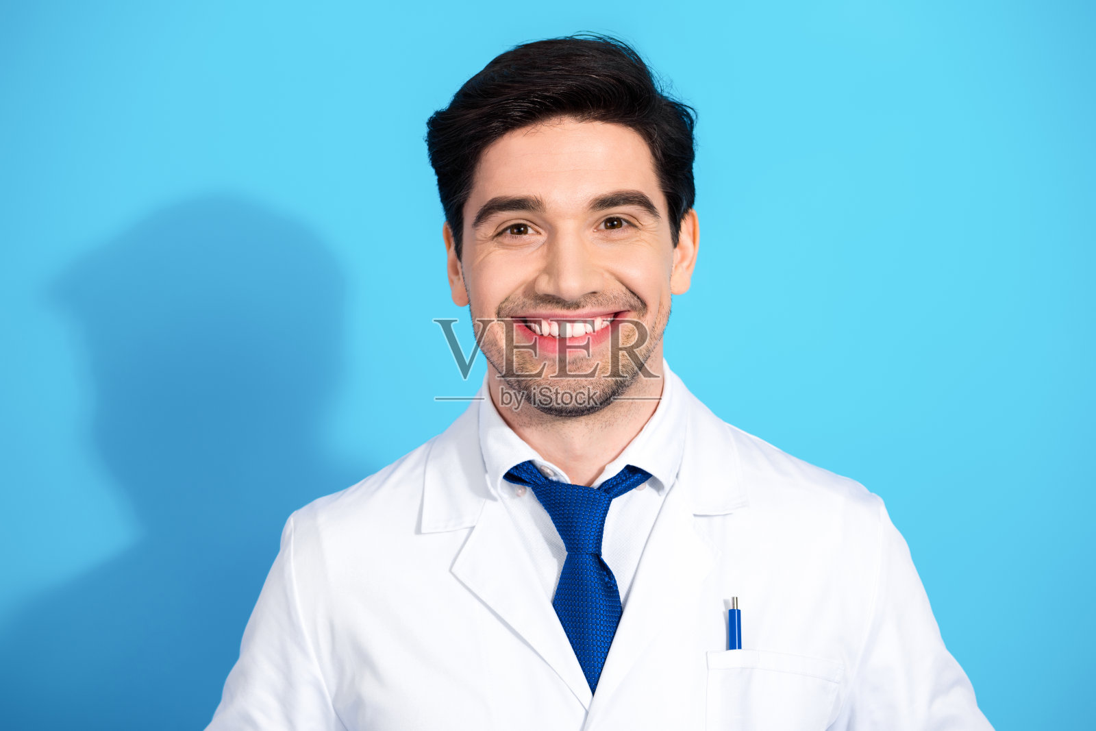 微笑的男性医生穿着白大褂，背景为蓝色，展现出自信和专业的医疗形象照片摄影图片