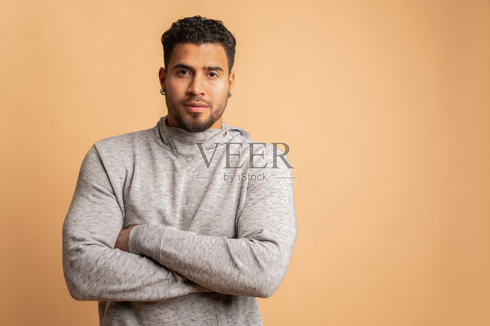 哥伦比亚男子交叉双臂，凝视镜头，背景为米色。照片摄影图片