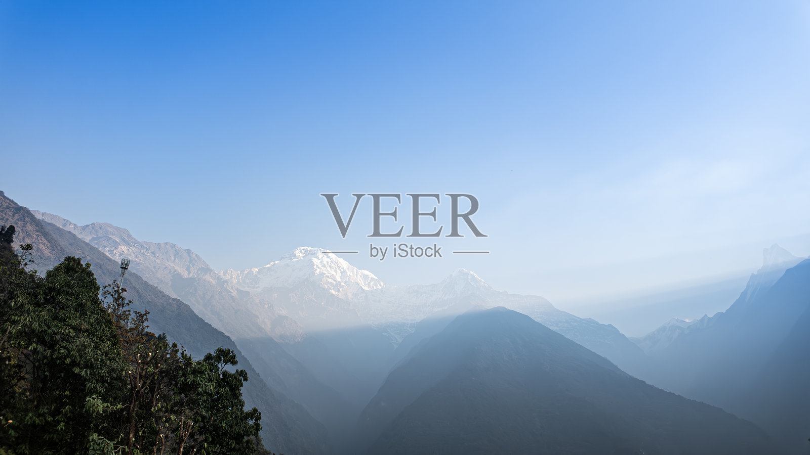 从尼泊尔安娜普尔纳大本营徒步旅行的乔莫朗观景点看到的雪山喜马拉雅山峰，背景是阳光射线、蓝天和白云。照片摄影图片