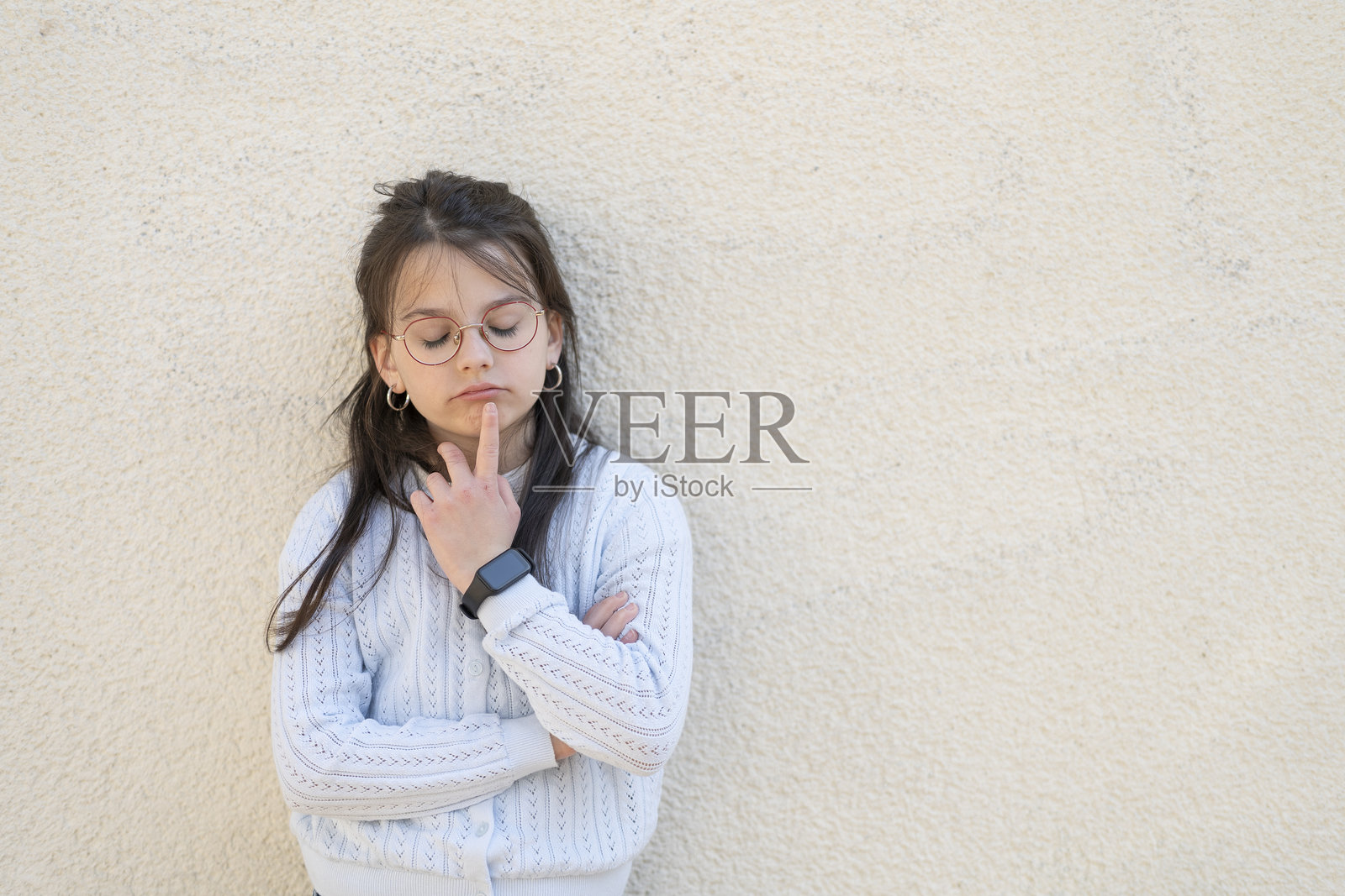 戴着红色眼镜的美丽女孩双臂交叉站在墙边。教育儿童的聪明孩子概念。照片摄影图片