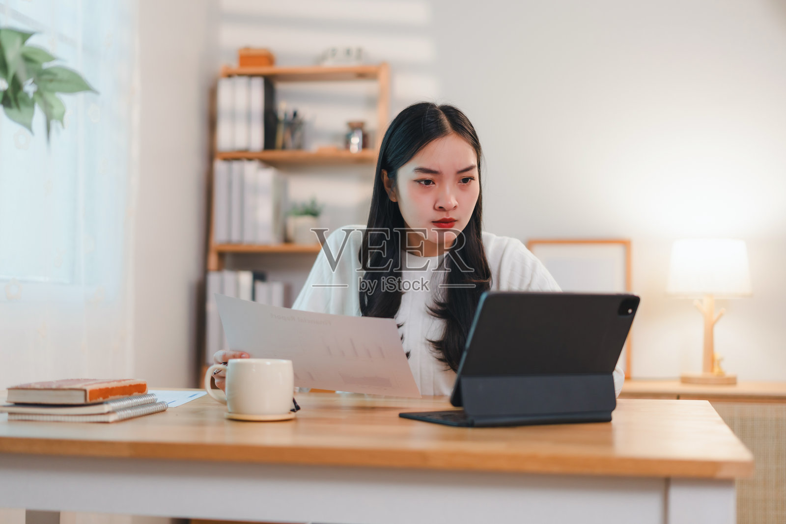 专注的女性在舒适的家庭办公室里使用平板电脑、纸张和咖啡杯工作照片摄影图片