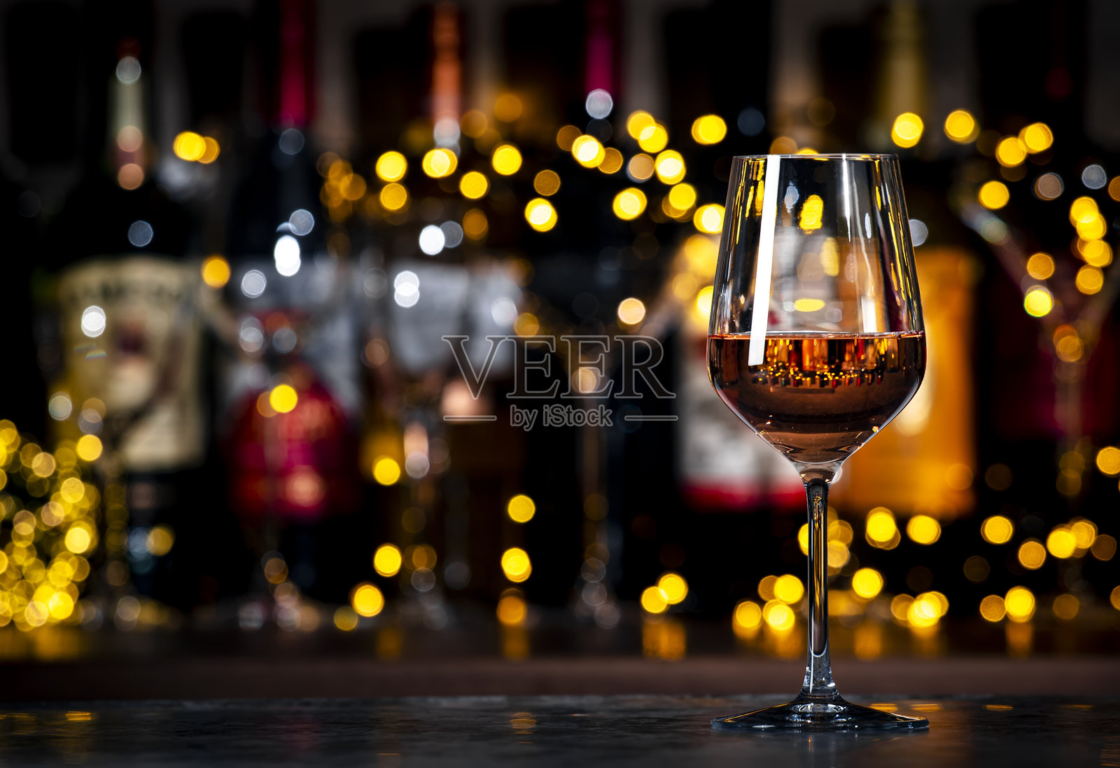 深色酒吧背景下，带有散景灯光的酒杯和酒瓶中的法国粉色安茹玫瑰酒照片摄影图片