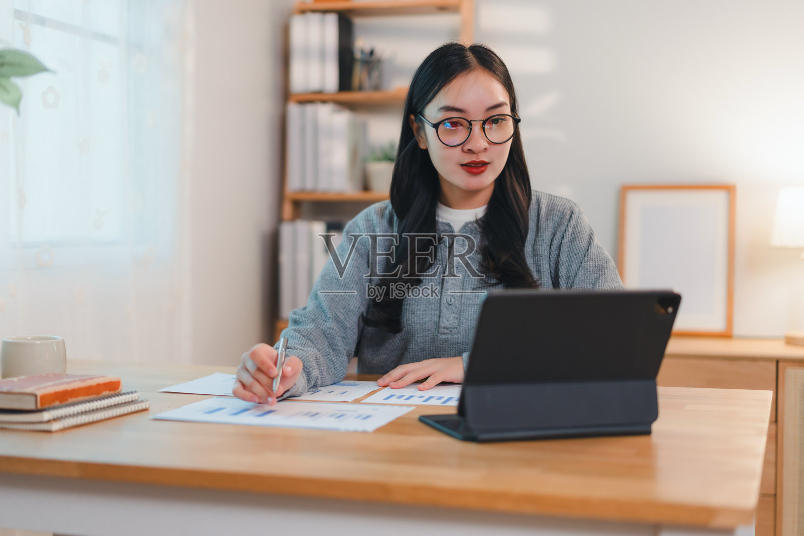 在明亮的家庭办公室里，女性在桌子上使用平板电脑分析文件。照片摄影图片