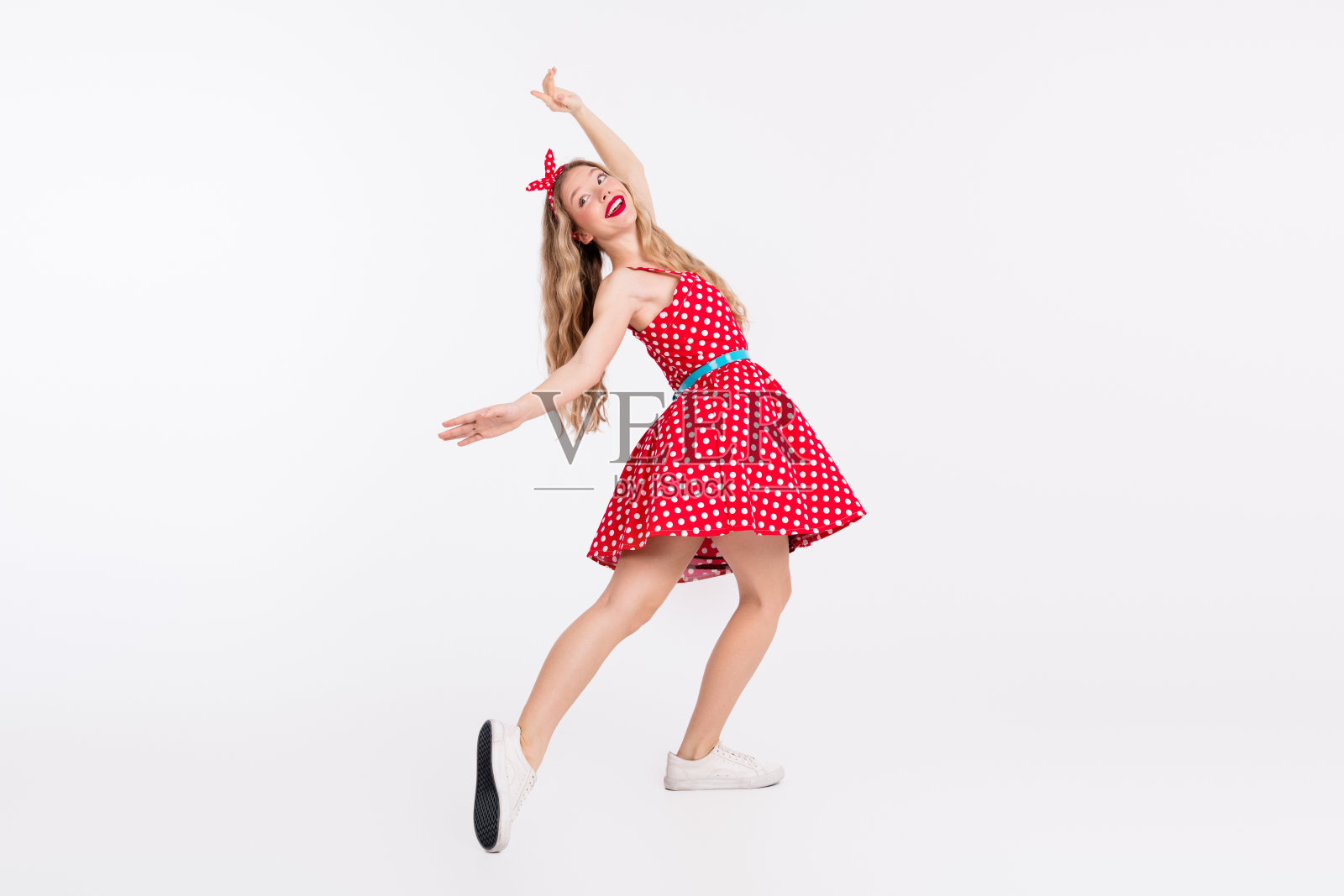 穿着复古红色波点裙的快乐金发女人在白色背景上跳舞照片摄影图片