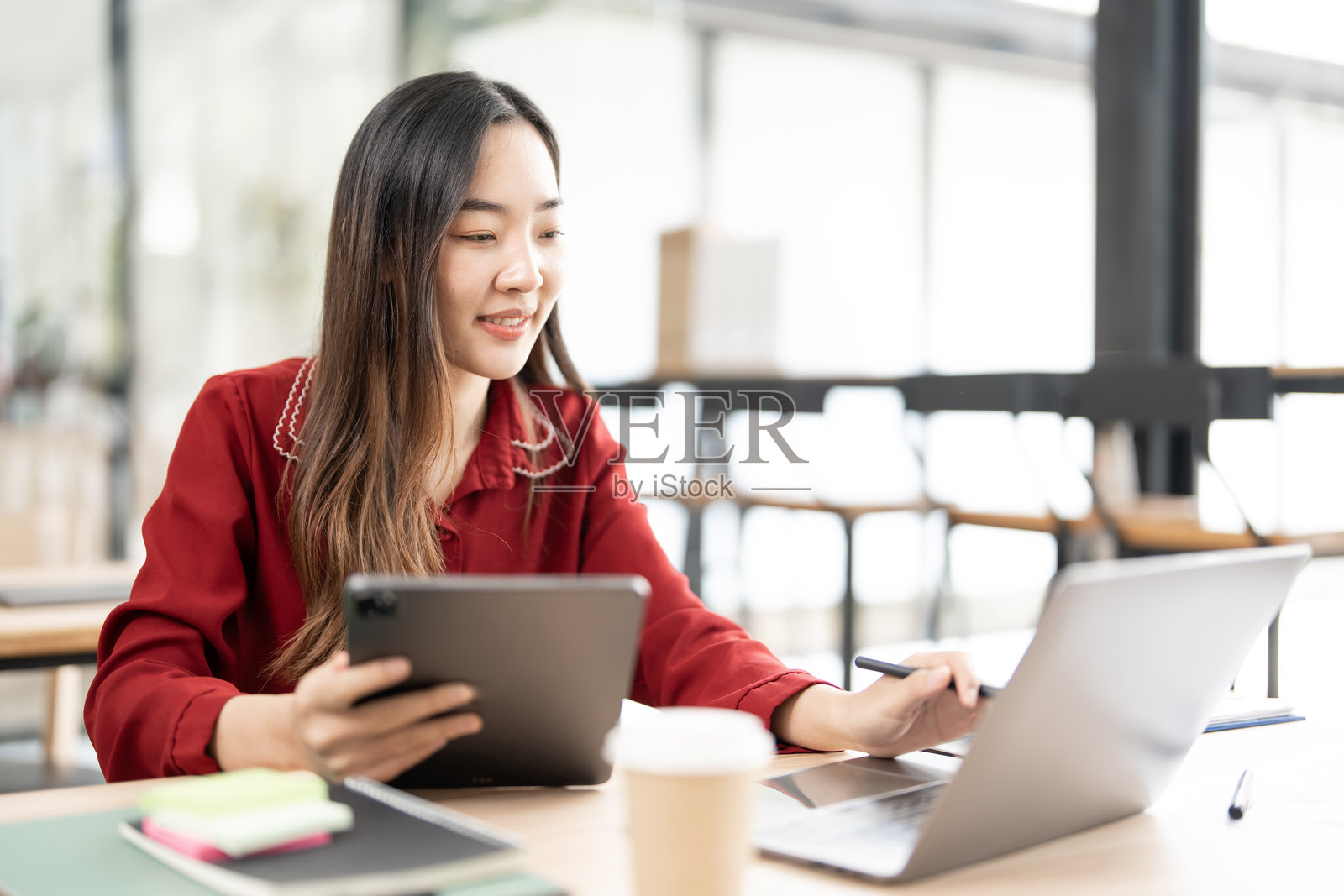 年轻的创意亚洲女性在办公室的桌子上使用数字平板和笔记本电脑。照片摄影图片