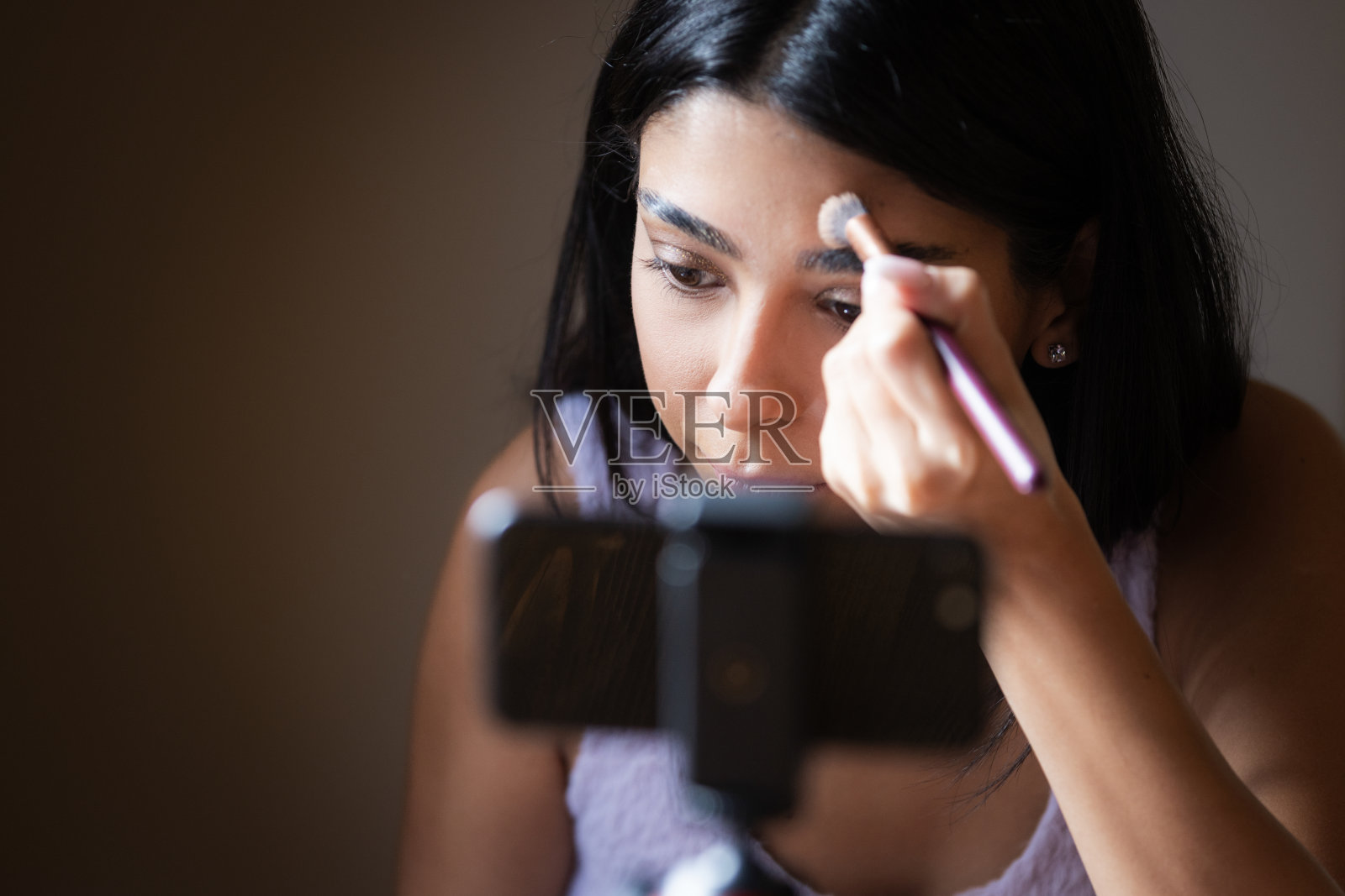 美容博主正在用智能手机录制视频，同时化妆。照片摄影图片