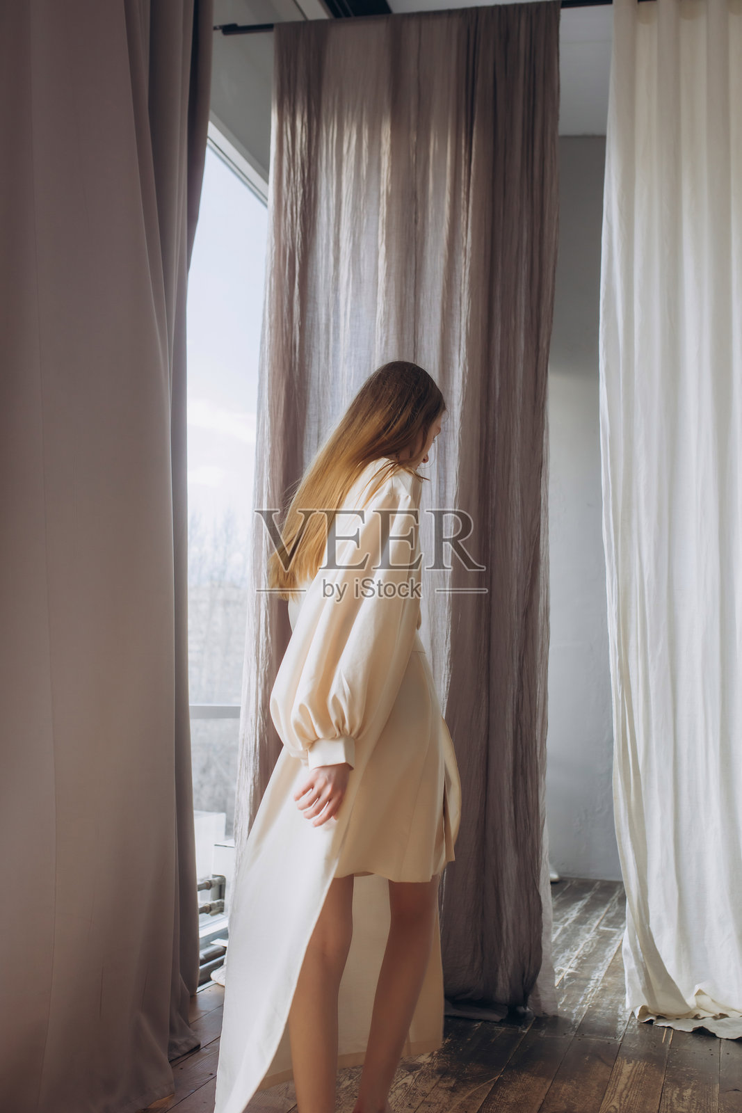 美丽的金发模特，年轻女孩，青少年，穿着飘逸面料的米色裙子在工作室里。照片摄影图片