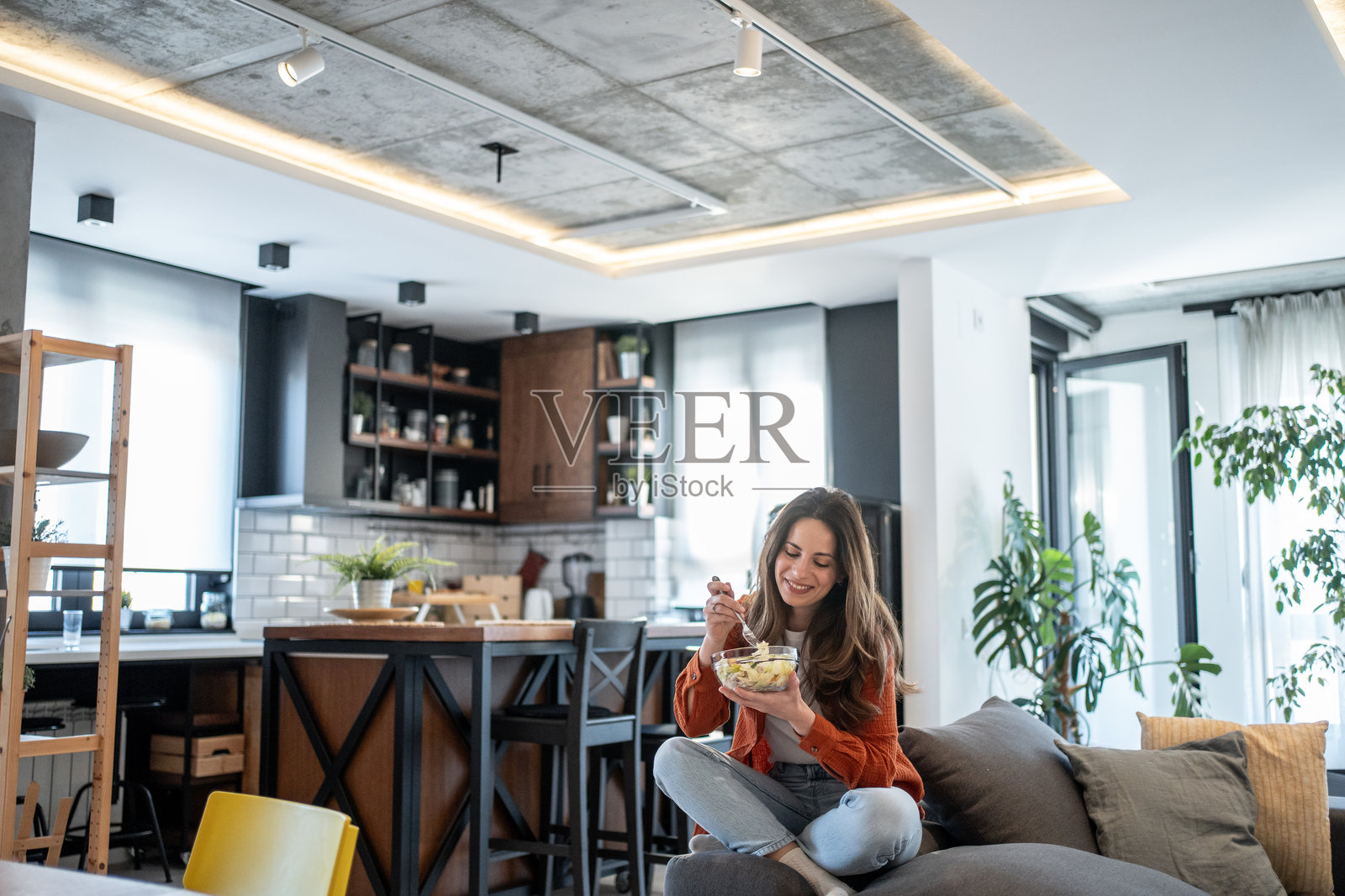 年轻女性在现代公寓的沙发上享用健康沙拉照片摄影图片