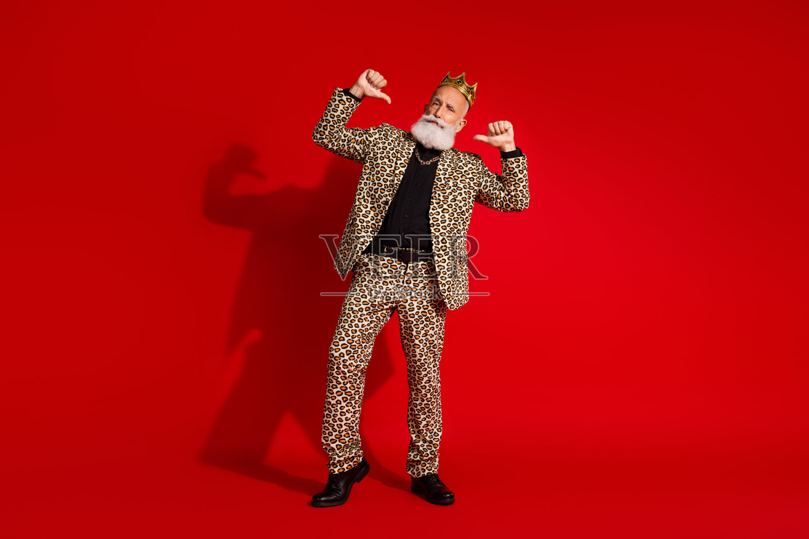 身穿豹纹西装的时尚老绅士在红色背景前自信地摆姿势，展现出玩乐和自信的姿态。照片摄影图片