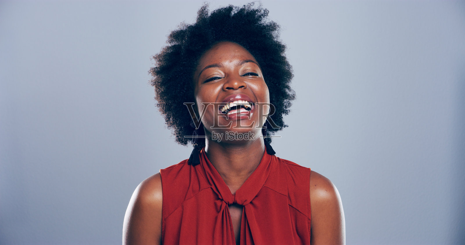 黑女人在蓝色背景的工作室中快乐地笑着，展现出幽默感，拥有自然卷发。兴奋、喜剧或积极情绪，展现出自豪或自信的非洲发型。照片摄影图片
