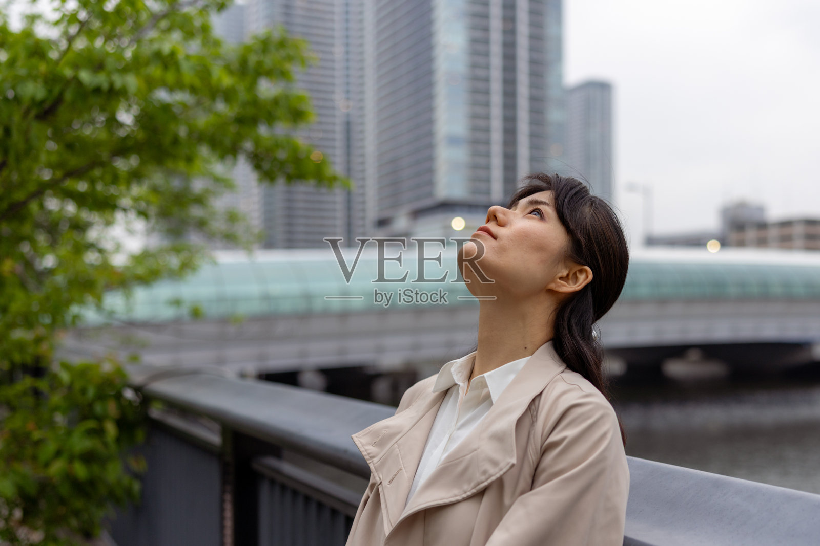 女商人在城市的河边站着 - 仰望天空照片摄影图片