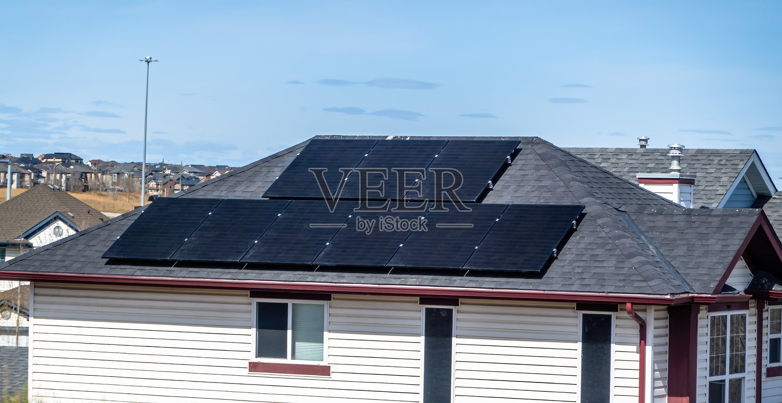 住宅屋顶上安装的太阳能电池板，背景是其他房屋和树木，天空多云。照片摄影图片