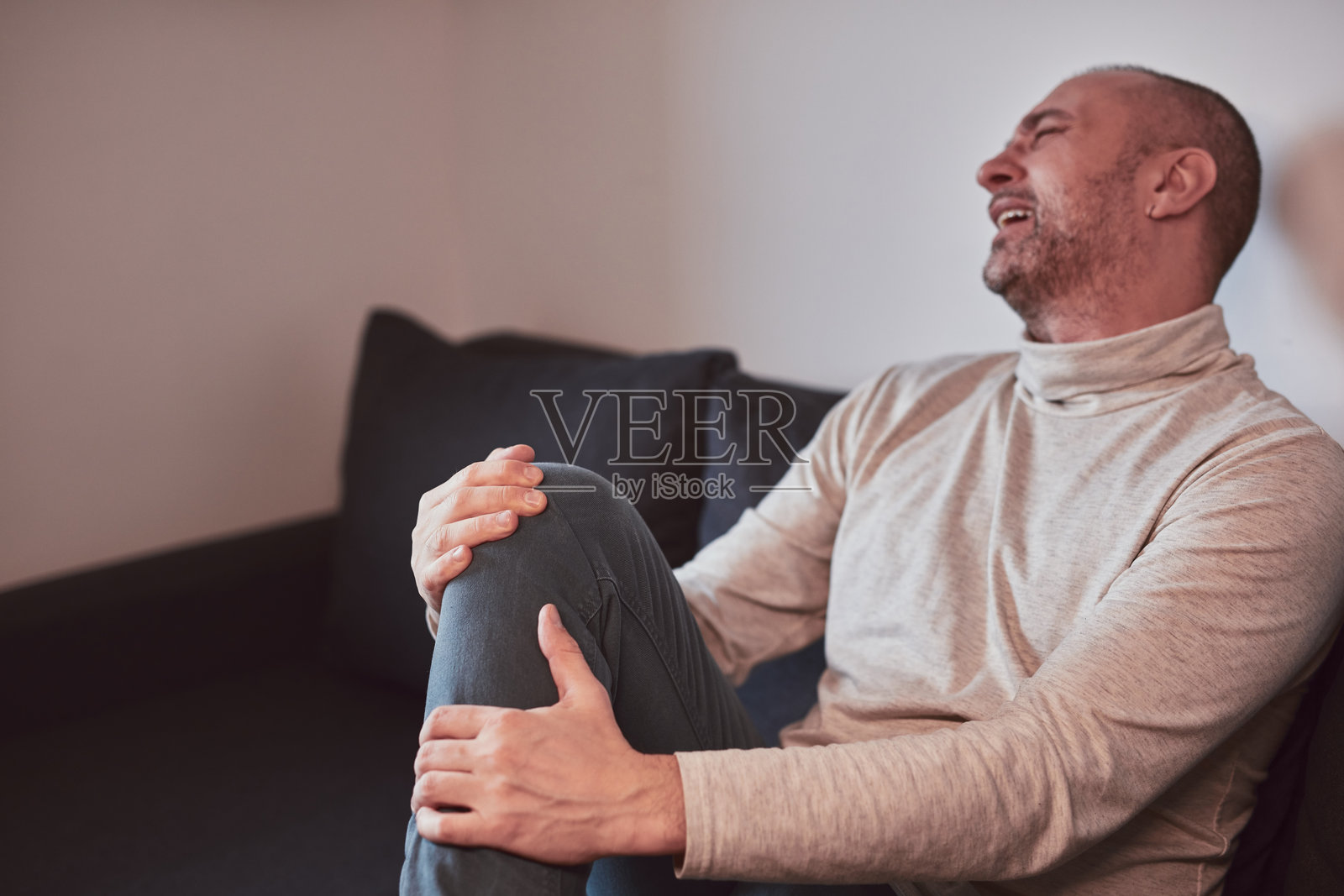 在家中膝盖和腿部受伤的男子感到疼痛。照片摄影图片