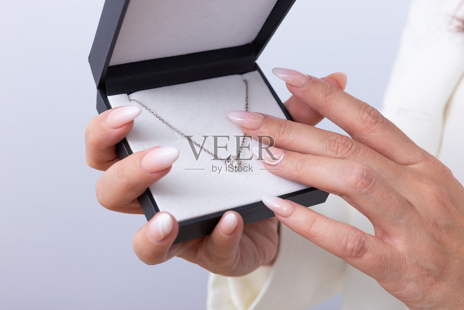 女性的手指做着法式美甲，展示着一个黑色盒子里的钻石项链。精美珠宝、特别礼物、优雅的概念。照片摄影图片