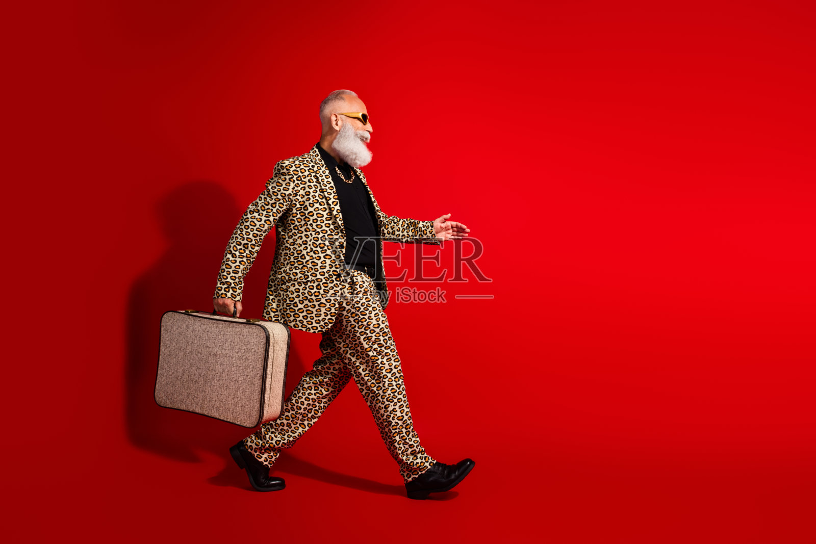 魅力四射的时尚模特，穿着豹纹西装，手提行李箱，背景为鲜艳的红色。照片摄影图片